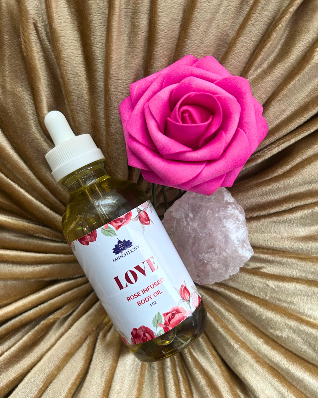 Bottle of 'LOVE' rose-infused body oil with a pink rose and crystal on a textured surface